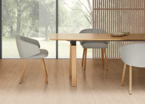 Sillones tapizados en gris con patas de madera junto a una mesa alargada frente a un ventanal al jardín