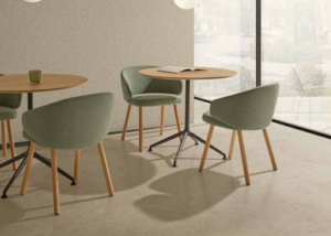 Sillones verdes con patas de madera en una zona de cafetería con mesas redondas