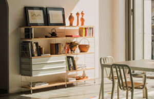Estantería modular de madera clara con libros, cajones blancos y objetos decorativos junto a una mesa de comedor