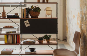 Estantería modular de madera oscura con módulo cerrado negro, libros y plantas ante un muro de piedra