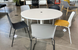Mesa redonda blanca con paso de cables y sillas apilables en gris, negro y amarillo