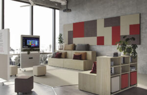 Aula flexible con sofá modular, paneles acústicos rojos y grises y pantalla móvil