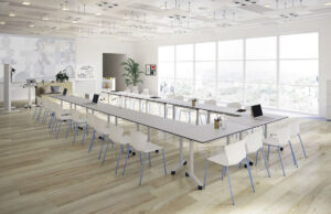 Sala de formación con mesas plegables blancas dispuestas en U y sillas apilables azules ante ventanales