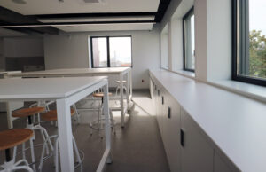 Sala junto a ventanales con mesas altas y mueble bajo corrido blanco