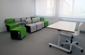 Butacas modulares verdes y grises con pala de escritura junto a mesa abatible