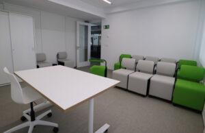 Aula con mesa abatible blanca y filas de butacas modulares verdes y grises