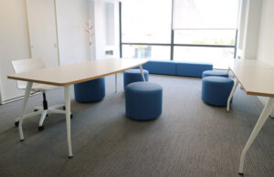 Sala con mesas abatibles, taburetes redondos azules y banco corrido azul junto al ventanal
