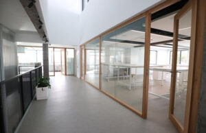 Pasillo con mamparas de vidrio y marco de madera junto a una sala de trabajo