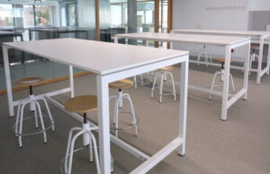Detalle de mesas altas blancas con taburetes regulables de asiento de madera