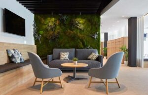 Zona de espera con jardín vertical, sofá gris y butacas con patas de madera