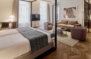 Habitación de hotel con cama, zona de estar con sofá y butacas y suelo de espiga