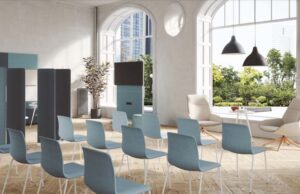 Sala de conferencias en un edificio de arcos con sillas azules apilables y pantalla