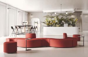Vestíbulo con sofá modular curvo rojo, mesas auxiliares y mesa alta al fondo