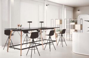 Mesa alta de tablero negro con taburetes y patas de madera en una zona diáfana