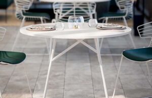 Detalle de mesa redonda blanca con vajilla y sillas verdes de rejilla metálica