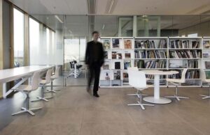 Biblioteca corporativa con mesas blancas, estanterías de revistas y una persona caminando