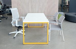 Mesa de reuniones blanca con estructura amarilla, silla operativa y sillas de visita