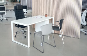 Mesa de despacho blanca con silla de dirección negra ante un panel de lamas de madera