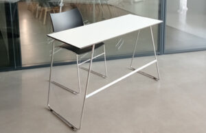 Mesa alta blanca con estructura cromada y silla negra junto a una mampara de vidrio