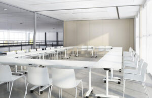 Sala de formación blanca con mesas plegables dispuestas en U y tabique móvil beis al fondo