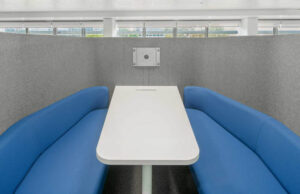 Interior de la cabina con dos bancos azules enfrentados, mesa blanca y soporte de pantalla