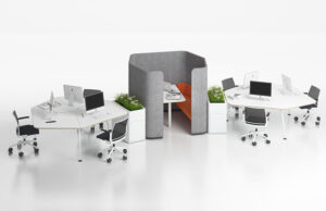 Puestos de trabajo hexagonales blancos en torno a una cabina acústica gris con jardineras