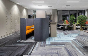Cabina acústica gris con asiento naranja en una oficina con taquillas y moqueta de diseño