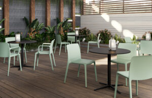Terraza de madera con sillas verde menta, mesas redondas negras y vegetación