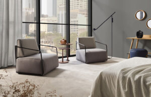Habitación de hotel con dos butacas grises, mesa auxiliar y vistas a la ciudad