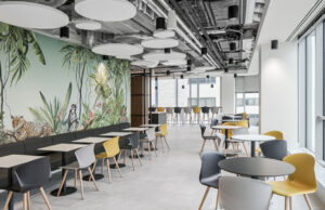 Cafetería con mural tropical, banco corrido, sillas grises y amarillas y plafones acústicos
