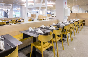 Comedor de autoservicio con mesas oscuras, sillas amarillas y bancos corridos
