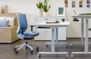 Mesa elevable blanca con ruedas y silla azul junto a un banco de madera