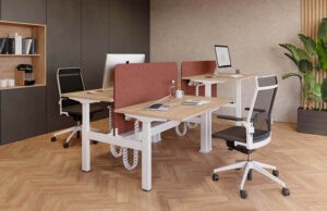 Dos mesas elevables de madera con separador rojo y sillas operativas en un despacho
