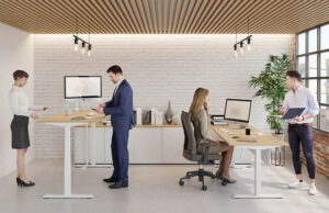 Oficina con cuatro personas trabajando, dos de ellas de pie ante mesas elevables