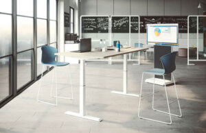 Mesa elevable en posición alta con taburetes azules ante ventanales y pizarra