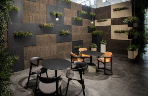Patio interior con paneles de corcho negro y beis con jardineras y mesas redondas