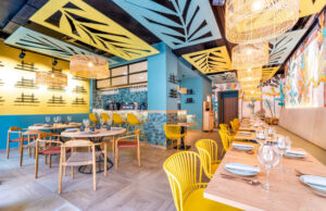 Restaurante con paneles calados amarillos y azules en el techo y sillas amarillas