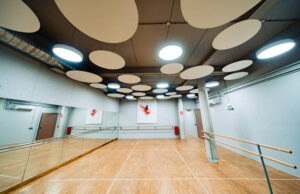 Sala de danza con plafones acústicos ovalados en el techo, espejos y barra