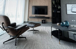 Salón con butaca de cuero y reposapiés ante una pared de lamas con televisor