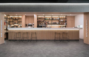 Bar cafetería con barra de madera retroiluminada, taburetes y estanterías de botellas