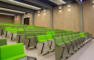 Auditorio con butacas verdes y paredes revestidas de lamas de madera