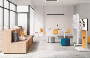 Grada de madera con cojines junto a mesas altas blancas, sillas amarillas y pantalla