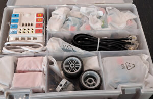 Maletín abierto con componentes de robótica: controladora, cables, ruedas y piezas