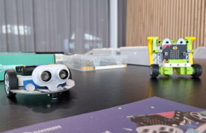 Dos robots con sensor de ultrasonidos sobre la mesa, con una placa micro:bit al fondo