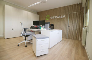 Despacho con mesa blanca, silla operativa y pared de lamas de madera con el logotipo de Gesvasa