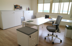 Despacho con mesa blanca en L, sillas de visita y cajonera con asiento tapizado