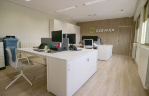 Sala con dos puestos dobles blancos, archivadores bajos y pared de lamas con el logotipo