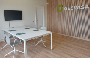 Sala de reuniones con televisor, mesa blanca y pared de lamas con el logotipo