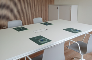 Mesa de reuniones blanca con carpetas corporativas y pared de lamas de madera