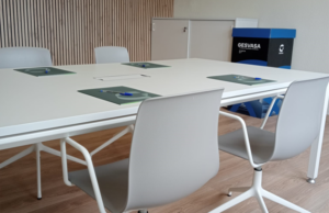 Mesa de reuniones con sillas blancas y contenedor de reciclaje corporativo al fondo